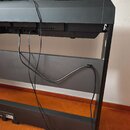 Zadní strana digitálního piana v černé barvě s přívukovou konstrukcí. V horní části jsou vidět konektory a nápisy, včetně textu "DIGITAL AUDIO OUT".…