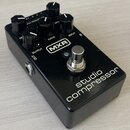 Černý efekt pedál s nápisy MXR a studio compressor. Na horní straně se nachází pět černých otočných ovladačů s bílými značkami a popisky RE, RATIO, A…