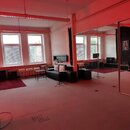 Interiér zkušebny s velkým zrcadlem na stěně a červeným osvětlením. V místnosti jsou rozmístěny hudební komba, černá pohovka, několik bílých stoliček…