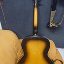 Zadní strana akustické kytary s barevným přechodem od žluté středu k černým okrajům. Hmatník a hlava jsou černé s bílými ladičkami. Na instrumentu ne…