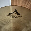 Detailní záběr na horní část mosazného činele. Na povrchu je černý nápis s logem „A“ a textem „MASTERSOUND HIHAT TOP 14"/36 cm“. Povrch vykazuje jemn…