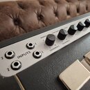 Detail horního ovládacího panelu kytarového komba v stříbrné barvě. Na panelu jsou tři vstupy s nápisem INPUTS a řada černých ovrtývakových knoflíků.…