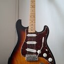 Elektrická kytara s trupem v barevnosti sunburst a javorovým hmatníkem. Nástroj má tři snímače s bílými krytkami, bílé ovládací knoflíky a červeně vz…