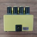 Žlutý efekt pedál s čtyřmi černými ovládacími knoflíky. Na spodní části je vstup pro napájení a bílý štítek s nápisem USE BOSS ACA ADAPTOR ONLY a sym…