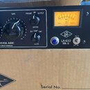 Černý rackový procesor s nápisy UNIVERSAL AUDIO a T4 Optical Compressor. Na předním panelu je žlutý VU metr, několik otočných ovladačů s popisky GAIN…