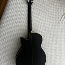 Zadní strana akustické kytary v matně černé barvě s hnědým lemováním. Na hlavě hmatníku je vidět logo s nápisem "YAMAHA". Nástroj vykazuje čistý povr…