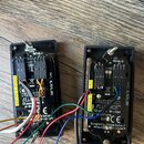 Dvě černé plastové krabičky s elektronickými součástmi a zapojeným barevným kabelázem. Na obou jsou vidět nápisy REV6.1 a REV6.0, logo FISHMAN FLUENC…