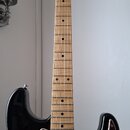 Elektrická kytara s trupem v černé a hnědé barvě (sunburst) a hnedým hmatníkem ze dřeva. Kytara má tmavě červený želvový pickguard a jeden viditelný…
