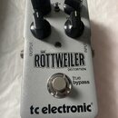 Stříbrný efekt pedál s nápisy RÖTTWEILER DISTORTION, true bypass a tc electronic®. Na horní části jsou čtyři černé oválné ovládací knoflíky a nápisy…