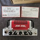 Kompaktní kytarový zesilovač v stříbrno-červené barvě s nápisy HEART ATTACK a NANO LEGACY stereo amplifier head. Zařízení má čtyři ovládací knofíky,…
