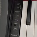 Detailní pohled na ovládací panel a část kláves digitálního pianina. Na černém plastovém panelu jsou tlačítka s nápisy DEMO/SONG, PIANO/VOICE, METRON…
