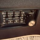 Detail ovládacího panelu s černým povrchem. Panel obsahuje čtyři posuvníky s označením hodnot -12, -6, 0, 6, 12 a nápis BATTERY. Vpravo je umístěn če…