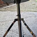 Černý polstrovaný bubeníckýstoliček s chromovanou kovovou konstrukcí a tříramenným stativem. Na středovém sloupku je viditelný nápis MAPEX a pod ním…