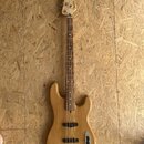 Elektrická basová kytara s přírodním dřevěným povrchem těla a hmatníku. Na hlavě je vidět nápis Fender. Instrument má čtyři struny, dva snímače a jed…