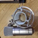 Stříbrný kondenzátorový mikrofon s mřížkou a doprovodným šokovým držákem z kovu. Na těle mikrofonu je nápis Apex4.35 a logo APEX. Povrch nástrojů je…
