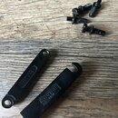 Na fotografii jsou dvě černé kovové součástky kobylky a čtyři černé šrouby. Na jedné součástce je vyražen nápis BM003, na druhé je logo a nápis GOTOH…