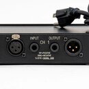 Detail zadní strany černého elektronického zařízení s konektory. Jsou zde vidět dva XLR konektory a nápisy INPUT, OUTPUT, CH 1 a text TIP=POSITIVE RI…