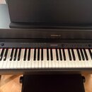 Černý digitální piano s klávesnicí a přívodním stojanem. Na horním panelu je nápis Roland a řada ovládacích tlačítek s popisky jako Function, Tempo,…
