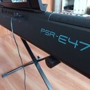 Černý digitální klavír umístěný na černém X-stojanu. Na pravé straně korpusu je modrý nápis PSR-E473 a vlevo bílé logo YAMAHA. Do přístroje je zapoje…