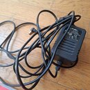 Černý síťový adaptér s dlouhým kabelem a konektorem typu jack. Na spodní straně je štítek s nápisy LINE 6, AC/DC ADAPTER, MODEL: HW-102500E, INPUT: 1…