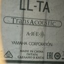Fotografie detailu štítku uvnitř akustické kytary. Na bílém podkladu jsou černým a zeleným písmem nápisy LL-TA, TransAcoustic v oválném rámu, A.R.E.)…