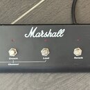 Černý obdélníkový ovládací panel s nápisem Marshall. Na přední straně se nachází pět stříbrných zapínacích tlačítek s popisky Clean, Crunch, Lead, Re…