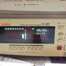 Detailní pohled na přední panel digitálního multitrackového nahrávače v krémové barvě. Na zařízení je uveden název značky Fostex a model D-80 s nápis…