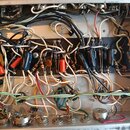Fotografie zachycuje vnitřek elektronického zařízení s hustou sítí barevných vodičů a zapojenými součástkami. Na černé desce jsou rozmístěny kondenzá…