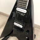 Černá elektrická kytara s triangulárním tvarem těla a hnědým hmatníkem. Nástroj má dva humbuckery s bílými plastovými krytkami, na kterých je u obou…