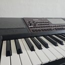 Detailní pohled na elektronický klavír v černé barvě. Na ovládacím panelu je nápis Pa700 a na plastovém rámu nad klávesami značka KORG. Nástroj má bí…