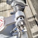 Detailní pohled na stříbrný kovový mechanismus basového pedálu s řetězem. Na boku je vidět červené kruhové logo s nápisy GERMAN a část slova ONOR. Po…