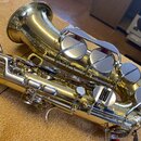 Detailní pohled na zlatý saxofon z horní perspektivy. Na zvonu je vidět nápis "MADE IN JAPAN". Nástroj vykazuje známky používání v podobě drobných šk…