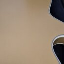 Zadní strana akustické kytary v matné zlatavé barvě. V horní části korpusu je umístěn černý plastový kryt elektroniky připevněný šrouby. Nástroj leží…