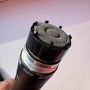 Detailní pohled na horní část černého dynamického mikrofonu. Na těle je bílý nápis SM58 a červené logo SHURE. Mikrofon nemá ochrannou mřížku, je vidě…