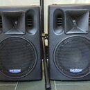Dva černé plastové aktivní reproduktory s integrovanými výšk SPEAKERY a velkými basovými membránami krytými kovovou mřížkou. Na spodní části obou rep…