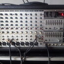 Stříbrošedý napájený mixážní pult v černém kufrovém pouzdře. Na předním panelu jsou nápisy BEHRINGER EUROPOWER, 2 X 250-WATTS STEREO POWERED MIXER WI…