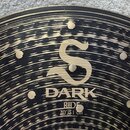 Detailní záběr na povrch činchy v barvě mosazi s černým, nepravidelným broušením. Uprostřed je zlaté logo ve tvaru stylizovaného písmene S a pod ním…
