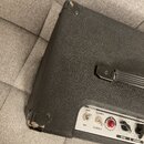Detailní pohled na černý kytarový kombozesilovač s texturovaným povrchem. Na ovládacím panelu jsou nápisy CRATE, 3 WATTS, OFF, ON, 5 WATTS, LITTLE GI…