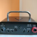 Černý kompaktní zesilovač s kovovou rukojetí. Na zadním panelu jsou nápisy PHONES / LINE, DC 19 V, ECO OFF ON STANDBY ON, EQ FLAT DEEP, IMPEDANCE 4 8…