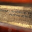 Detailní záběr na vnitřní štítek smyčcového nástroje. Na zažloutlém, zaprášeném papíře je černý nápis Antonijus Stradivarius Cr Faciebat anno 17. Pov…