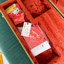 Otevřený kufřík s červeným plyšovým vnitřkem. V úložných přihrádkách se nachází několik papírových štítků, dokumentů a červený obal s bílým nápisem F…