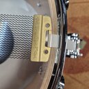 Detailní záběr na kovový mechanismus upevnění bubnu. Na zlatavém kovovém držáku je vyražen nápis "dw TravelTone dwl". Součástí je chromovaný obruč a…