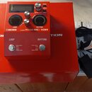 Červený loop pedal s nápisy BOSS, RHYTHM LOOP STATION a RC-10R. Zařízení má displej, několik ovládacích knoflíků a dva stoupací spínače s popisky LOO…