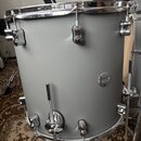 Šedý buben s chromovanými obručemi a mechanismy. Na korpusu je umístěn oválný kovový štitek s nápisem „Concept drums“. Povrch nástroje je matný a v d…