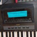 Detailní pohled na ovládací panel a klávesy elektronického klavíru. V horní části je podsvícený modrý displej s texty jako Pat, Chd, Tmr a Load Save.…