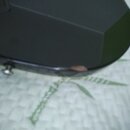 Detailní záběr na černý, lesklý povrch hudebního nástroje. Na hraně těla je vidět odštípnutý kousek laku, který odhaluje světlejší podklad. V levé čá…