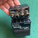 Černý efekt pedál s nápisy Bass Driver BB-1X a logem BOSS. Na horní části jsou čtyři ovládací knoflíky s popisky LEVEL/BLEND, LOW, HIGH a DRIVE, nad…
