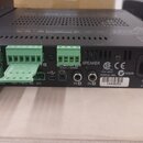 Zadní strana černého elektronického zařízení s několika konektory. Jsou zde zelené šroubovací svorkovnice, USB port a dva vstupy označené IN 1 a IN 2…