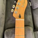Hmat krku a hlavy elektrické kytary z přírodního dřeva v šedém obalu. Na hlavě je vidět nápis Fender a TELECASTER®. Kytara má šest chromovaných ladič…