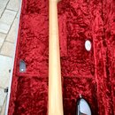 Zadní strana krku a části těla basové kytary v tvrdém kufru s červeným plyšovým vnitřkem. Na těle je vidět nápis Fender a povrch s přechodem barev od…